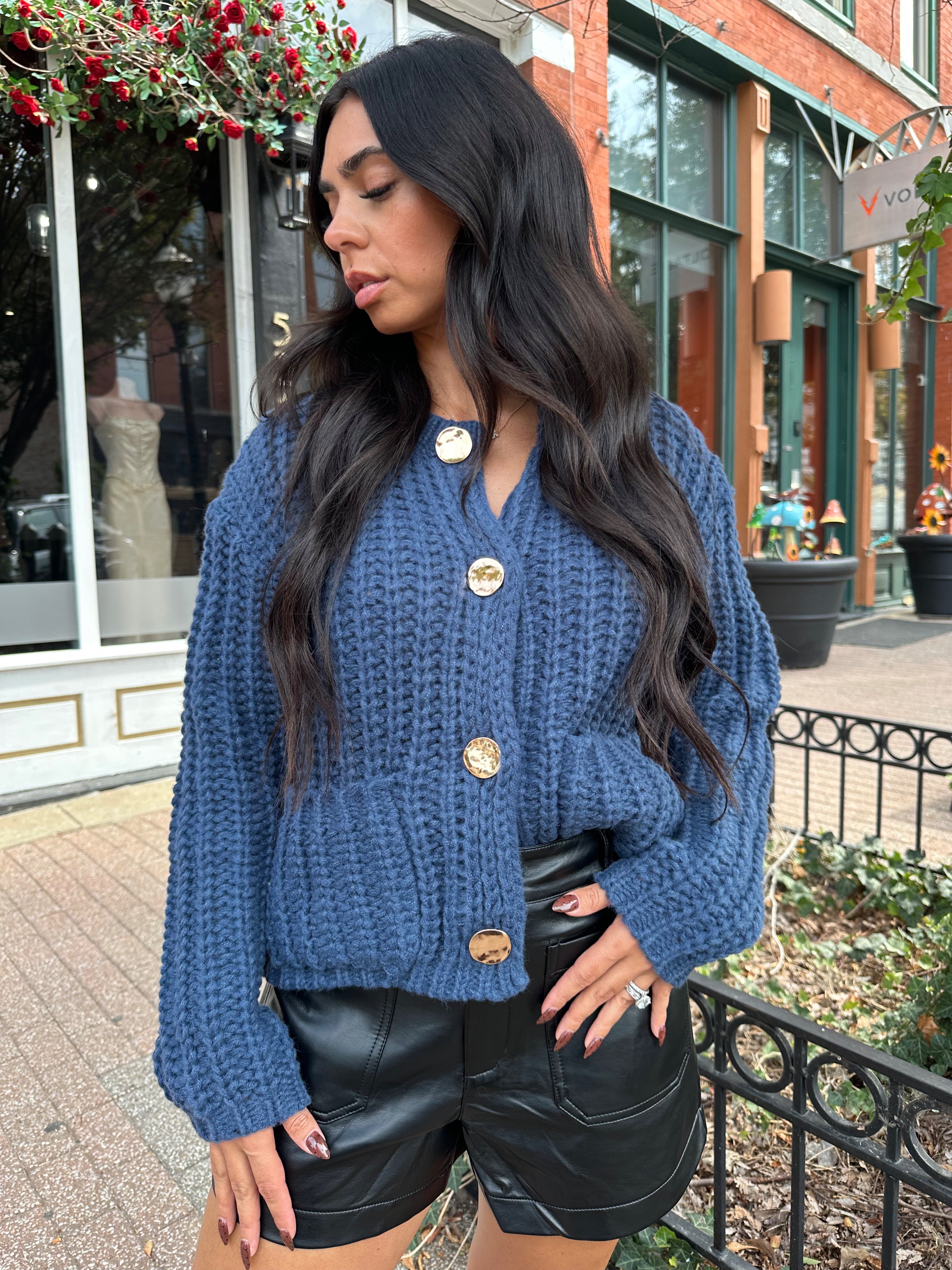 Woman wearing dark blue chunky cardigan with gold button closure. 