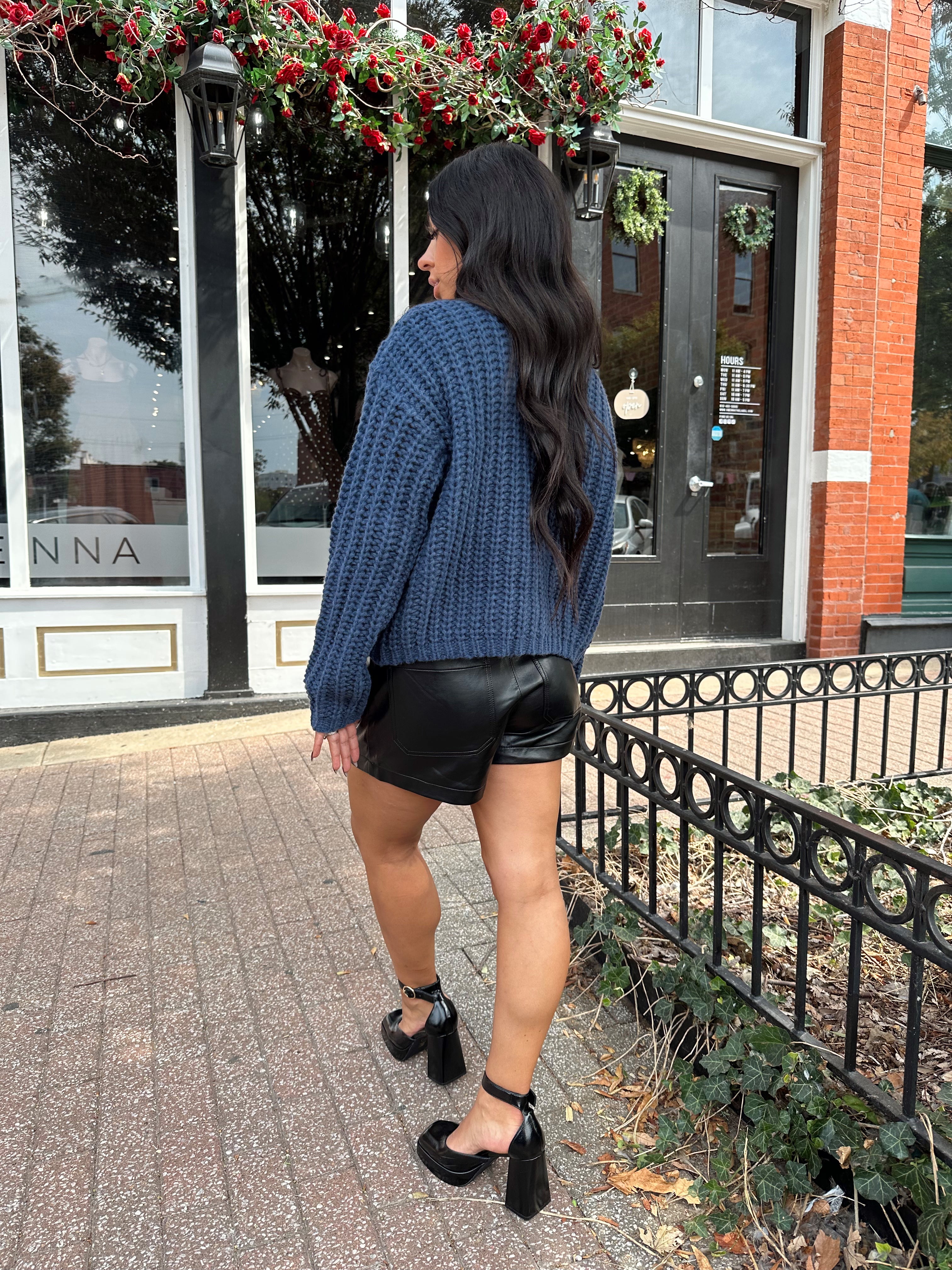 Woman wearing dark blue chunky cardigan with gold button closure. 