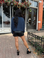 Woman wearing dark blue chunky cardigan with gold button closure. 