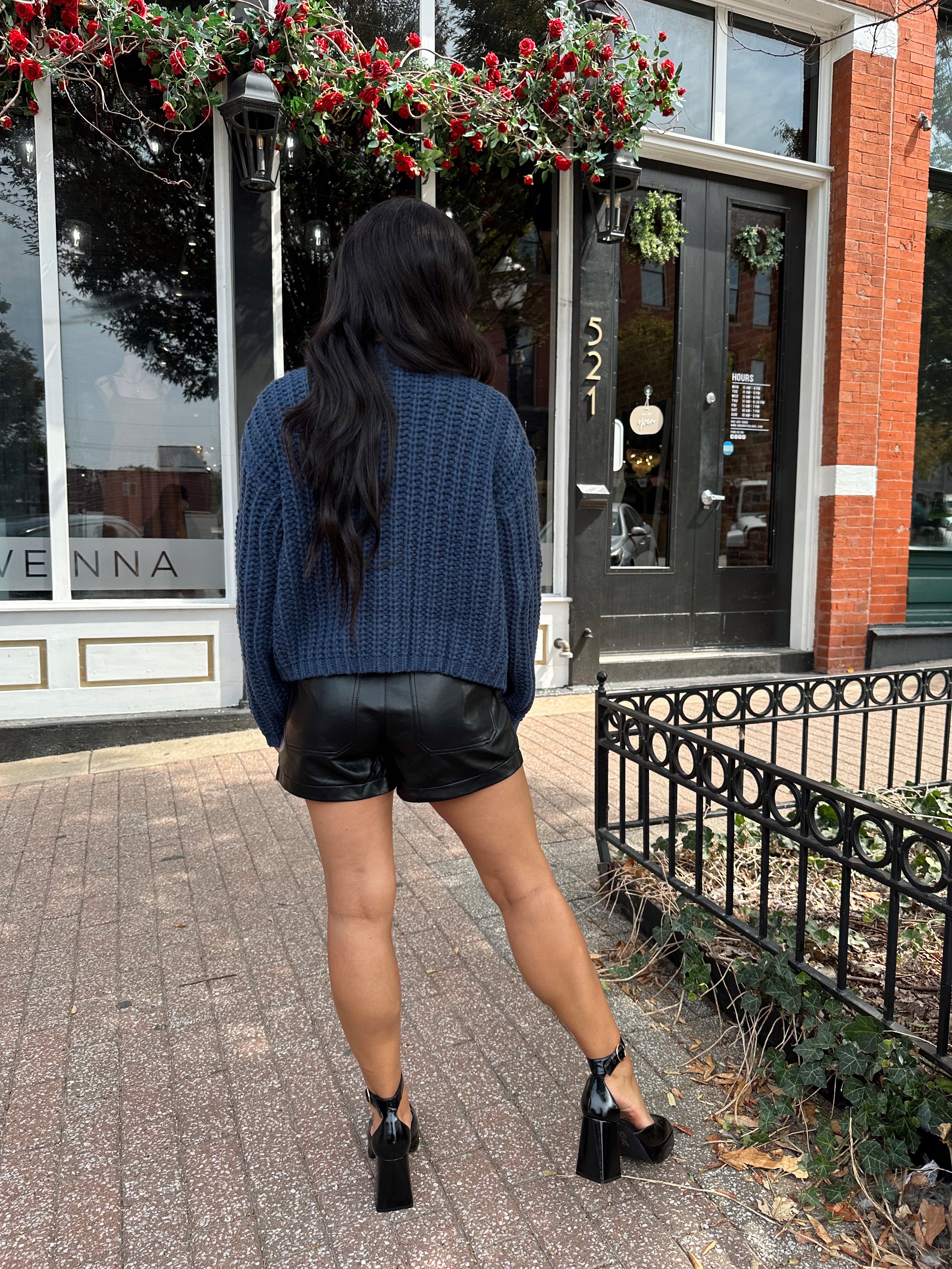 Woman wearing dark blue chunky cardigan with gold button closure. 