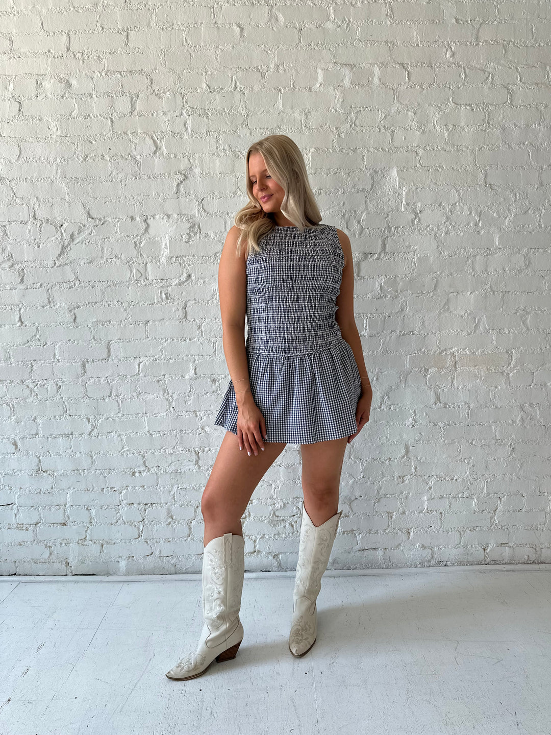 Woman wearing navy gingham smocked mini dress with built in shorts.