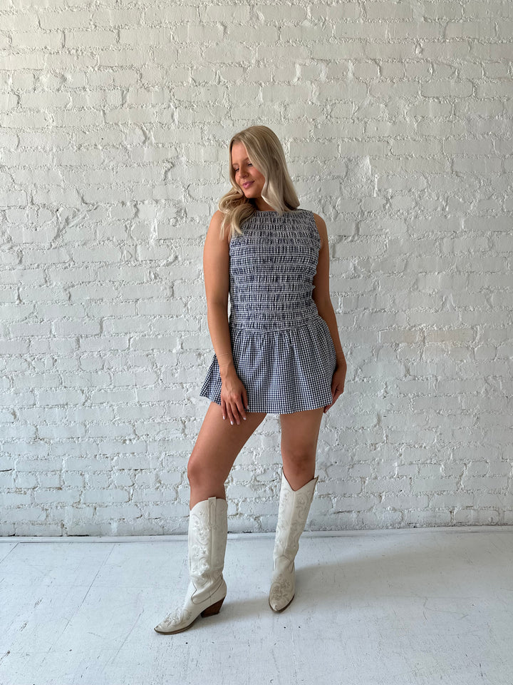 Woman wearing navy gingham smocked mini dress with built in shorts.