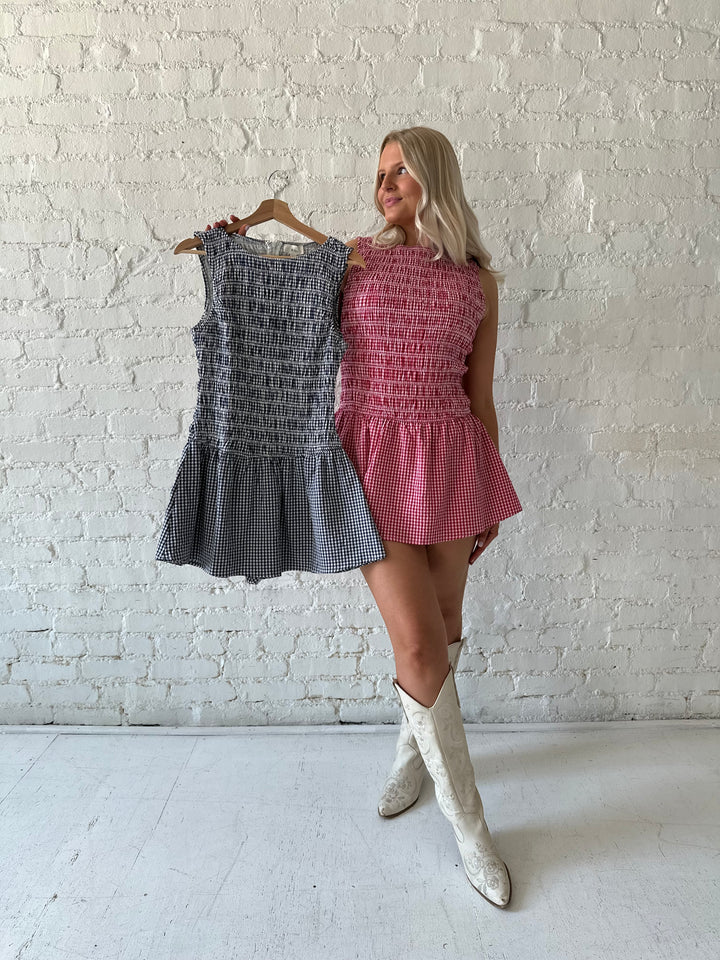 Woman wearing navy gingham smocked mini dress with built in shorts.