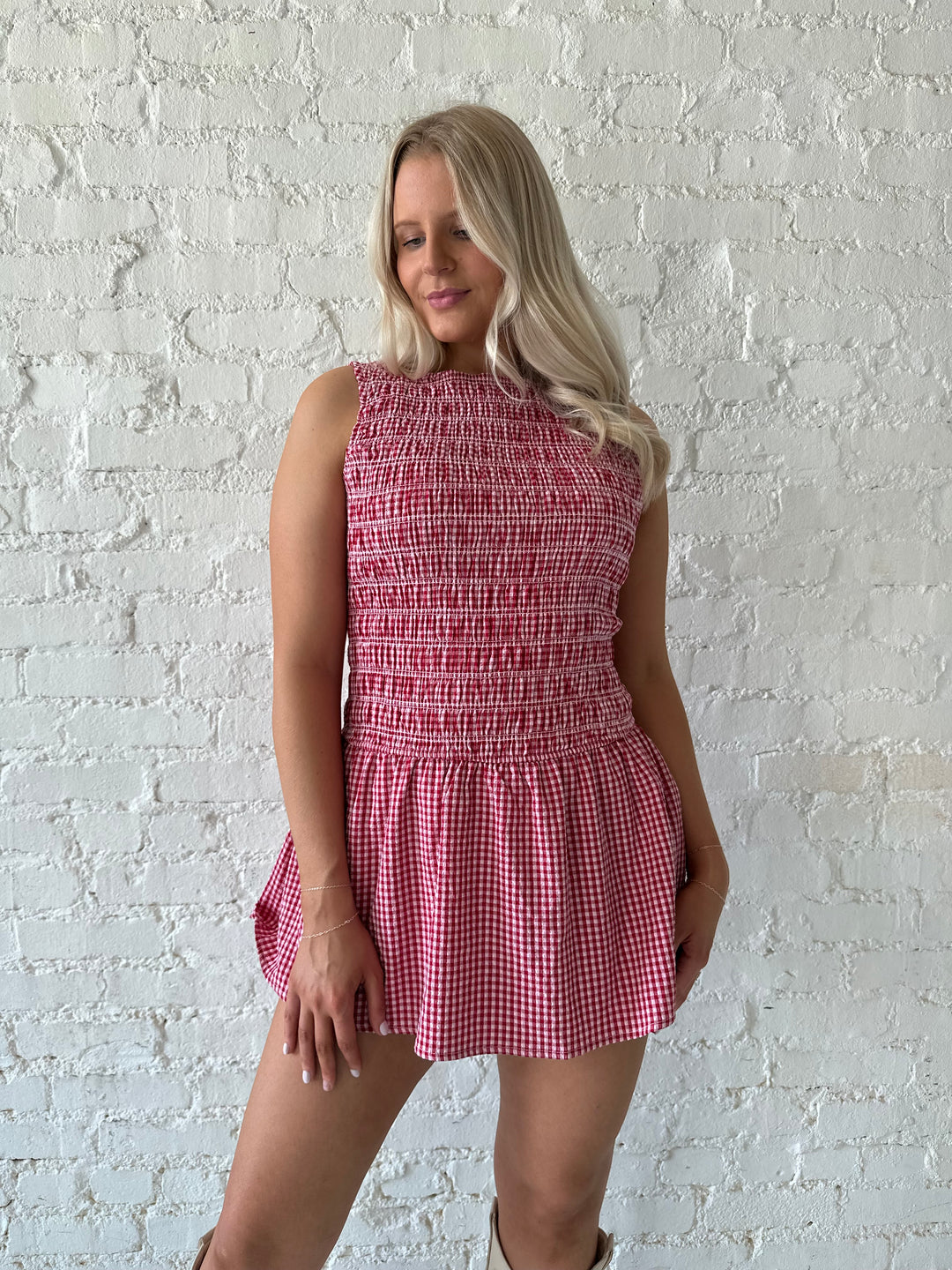Woman wearing red gingham smocked mini dress with built in shorts.