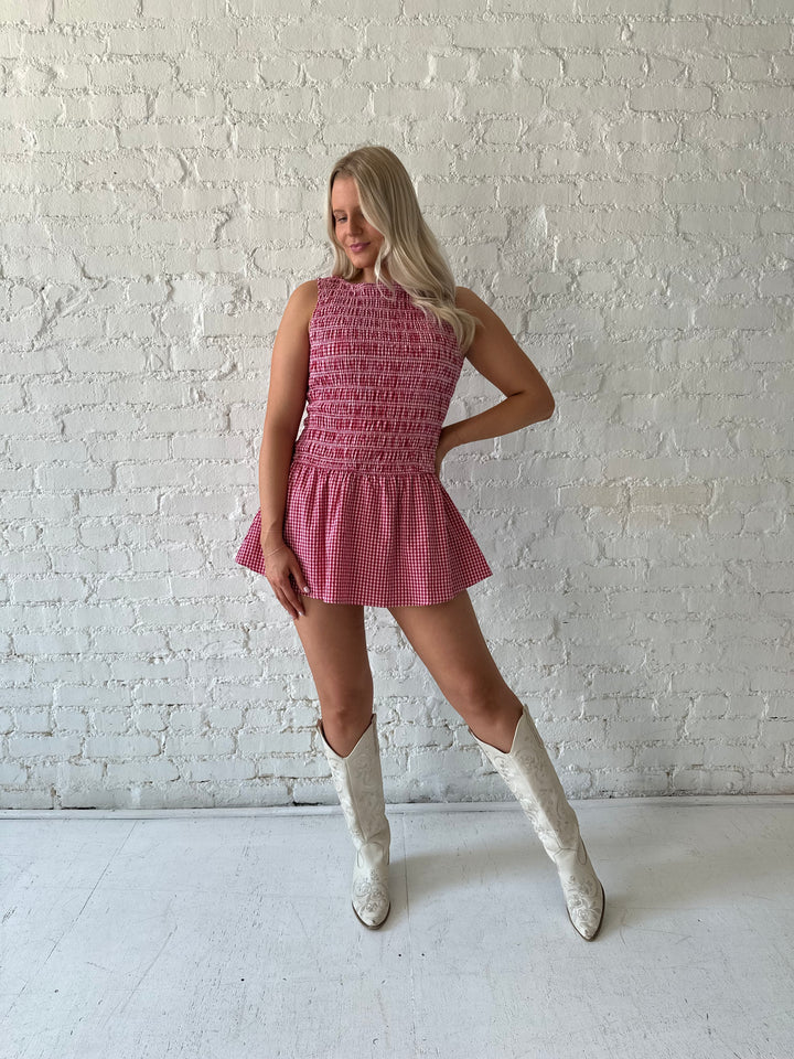 Woman wearing red gingham smocked mini dress with built in shorts.