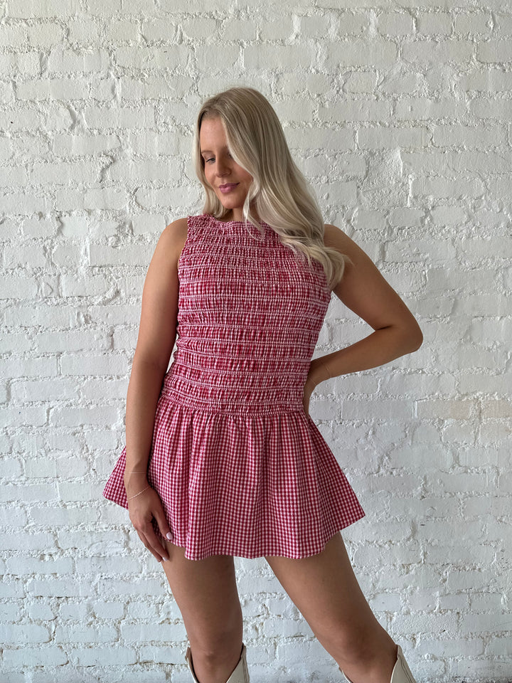 Woman wearing red gingham smocked mini dress with built in shorts.