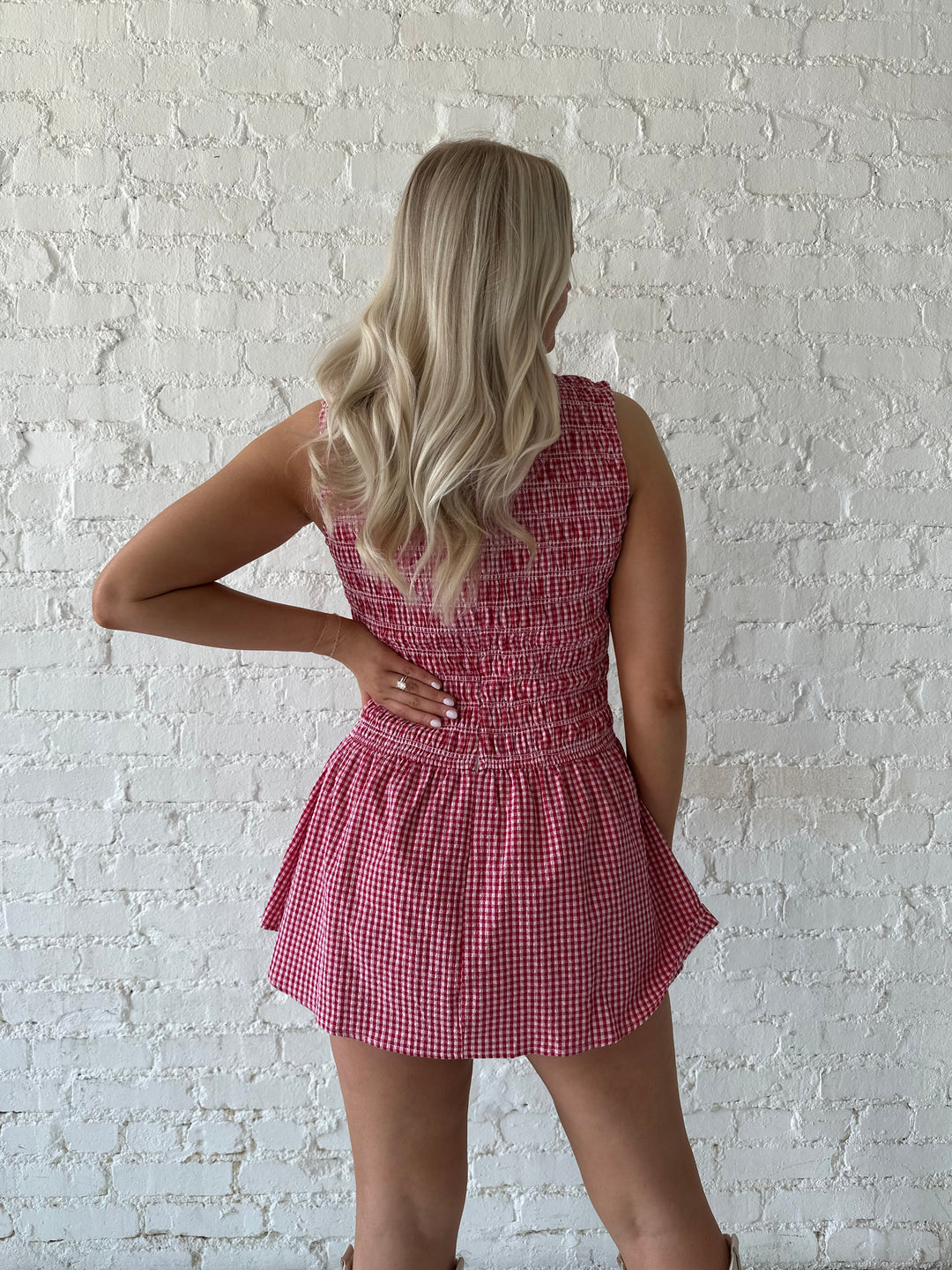 Woman wearing red gingham smocked mini dress with built in shorts.