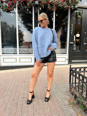 Woman wearing light blue knit sweater with front pockets, and leather shorts.