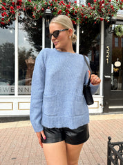 Woman wearing light blue knit sweater with front pockets, and leather shorts.