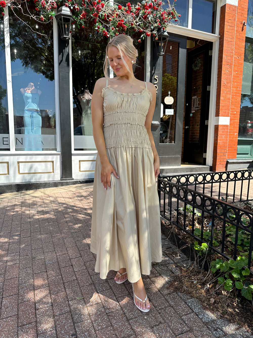 Woman wearing tan maxi dress with smocked bodice, adjustable spaghetti straps, and side slit. 