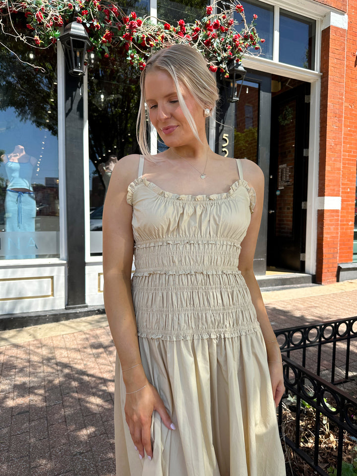 Woman wearing tan maxi dress with smocked bodice, adjustable spaghetti straps, and side slit. 