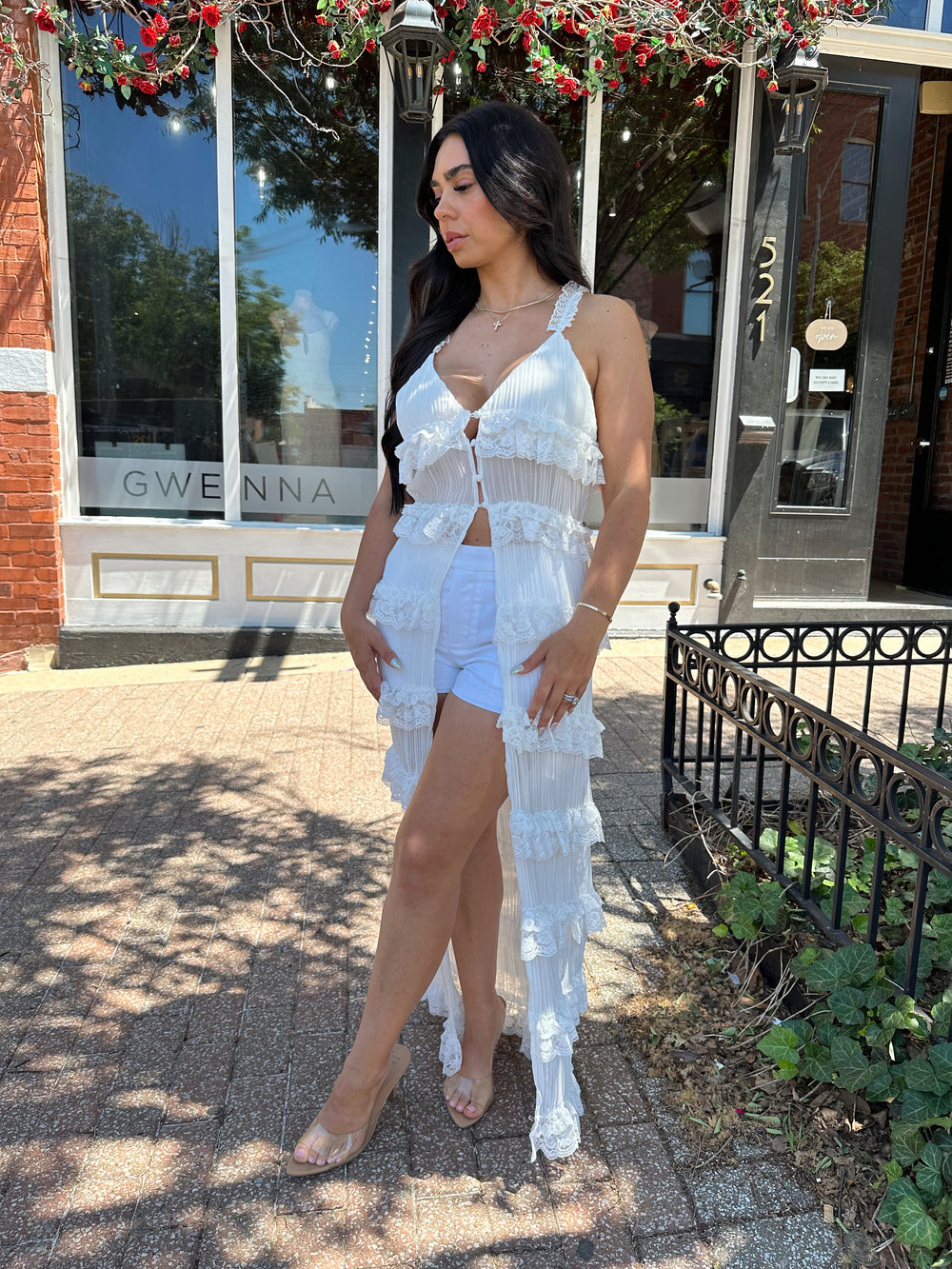 Woman wearing white sheer overlay duster with ruffle tiered detailing, and button closure.