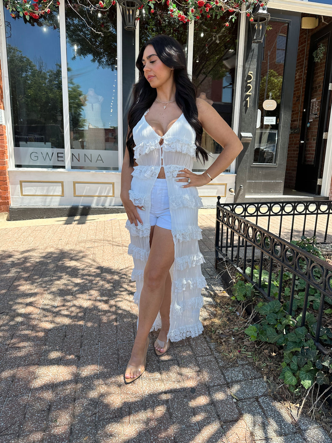 Woman wearing white sheer overlay duster with ruffle tiered detailing, and button closure.