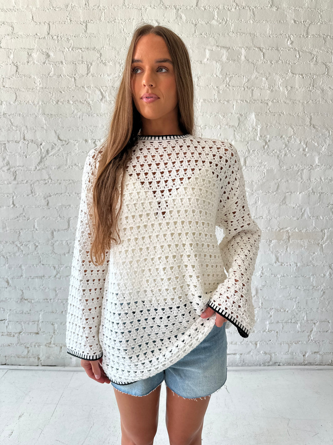 Woman wearing white crochet tunic top with black trim detailing and tie back. 
