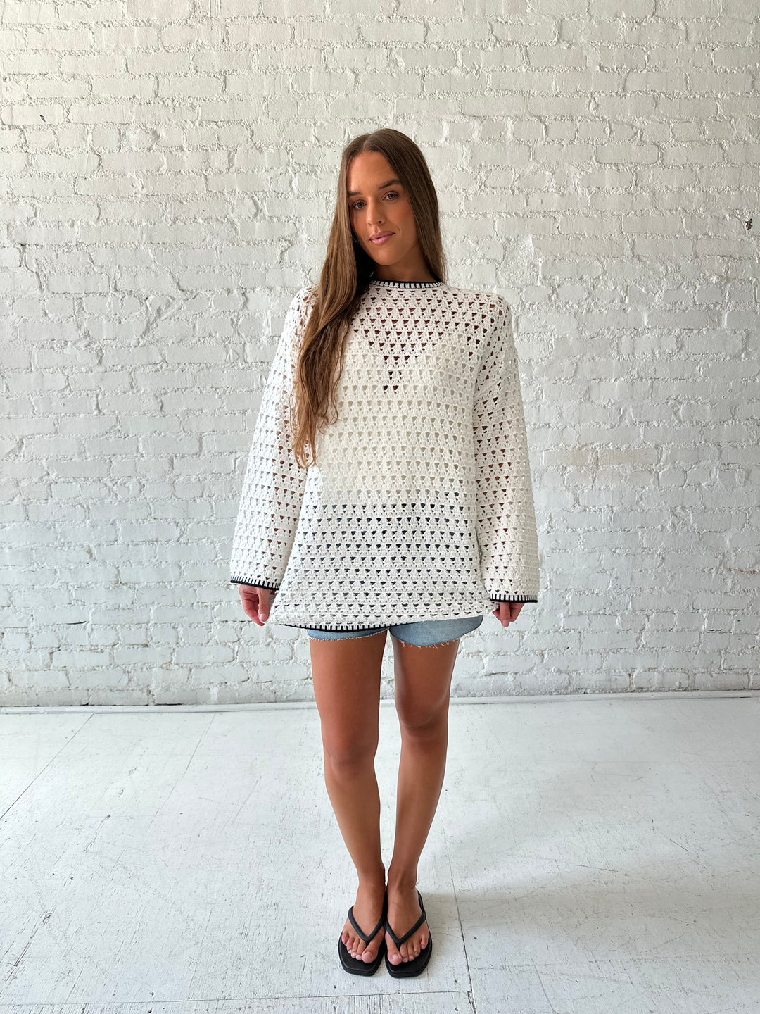 Woman wearing white crochet tunic top with black trim detailing and tie back. 