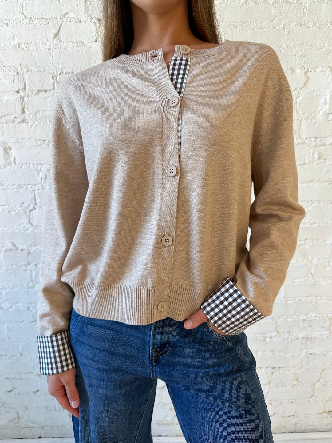 Woman wearing beige knit cardigan with gingham trim, and dark wash jeans.