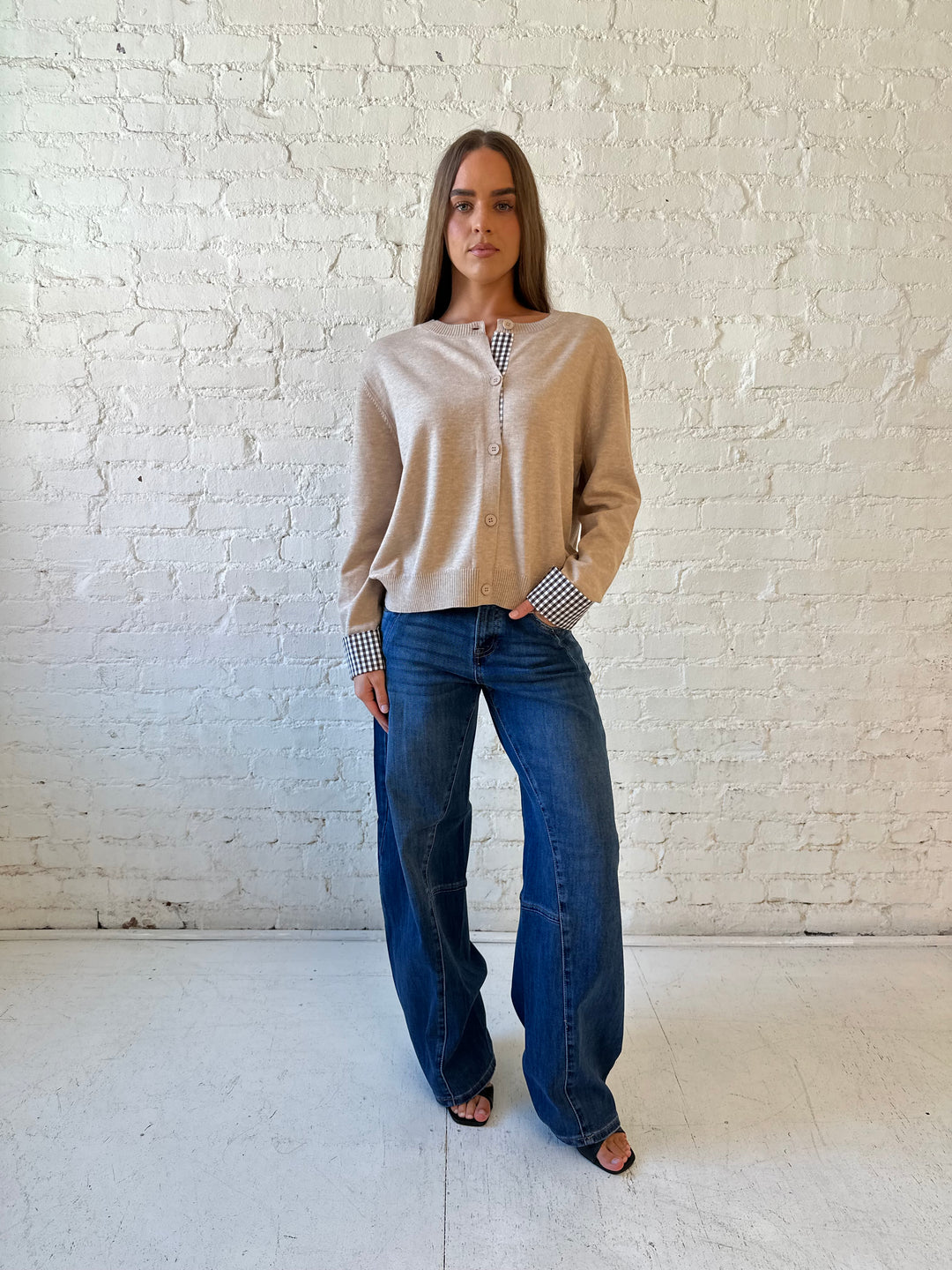 Woman wearing beige knit cardigan with gingham trim, and dark wash jeans.