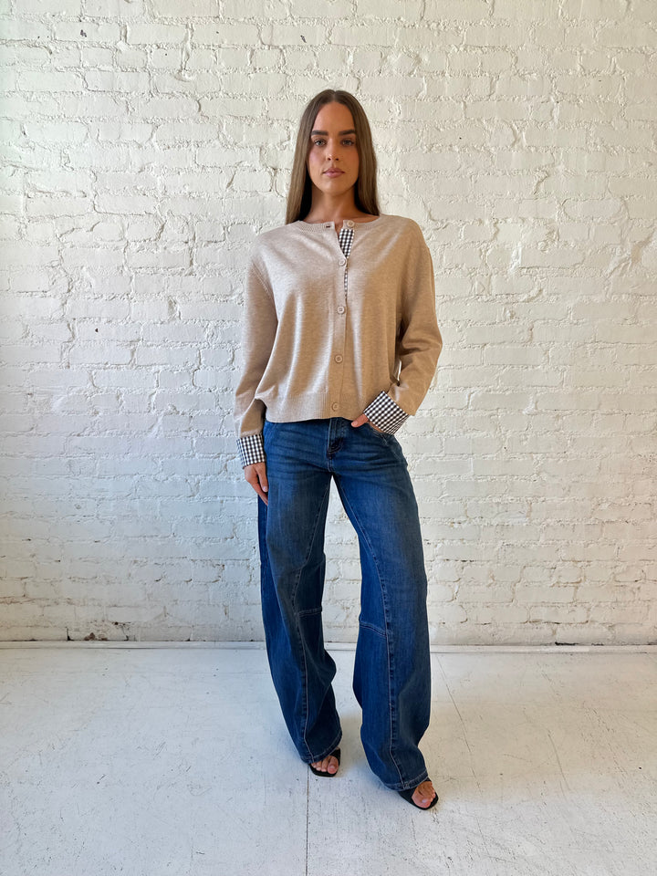 Woman wearing beige knit cardigan with gingham trim, and dark wash jeans.