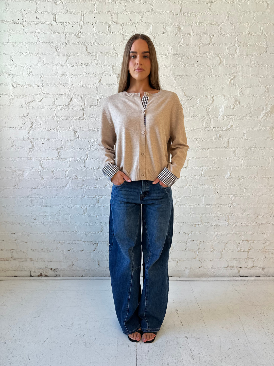 Woman wearing beige knit cardigan with gingham trim, and dark wash jeans.