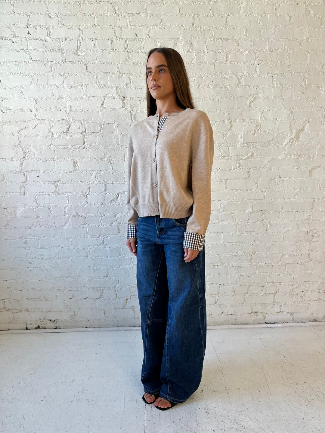 Woman wearing beige knit cardigan with gingham trim, and dark wash jeans.