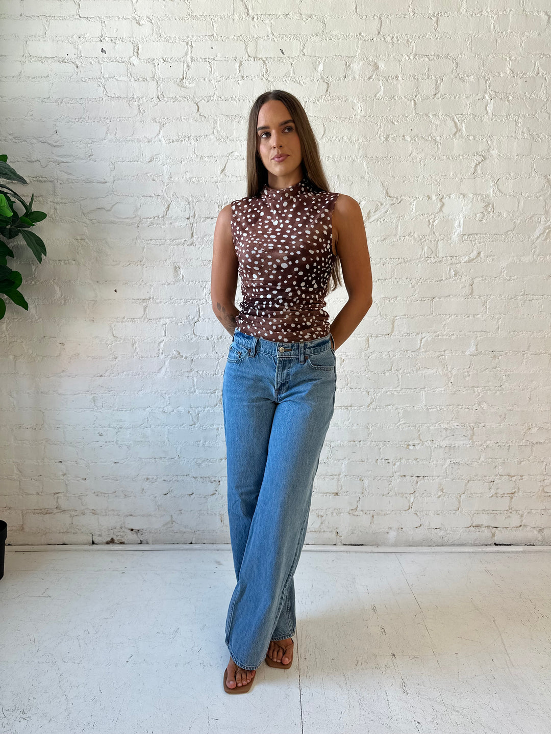 Woman wearing fawn print mesh sleeveless top with high neckline and medium wash jeans. 