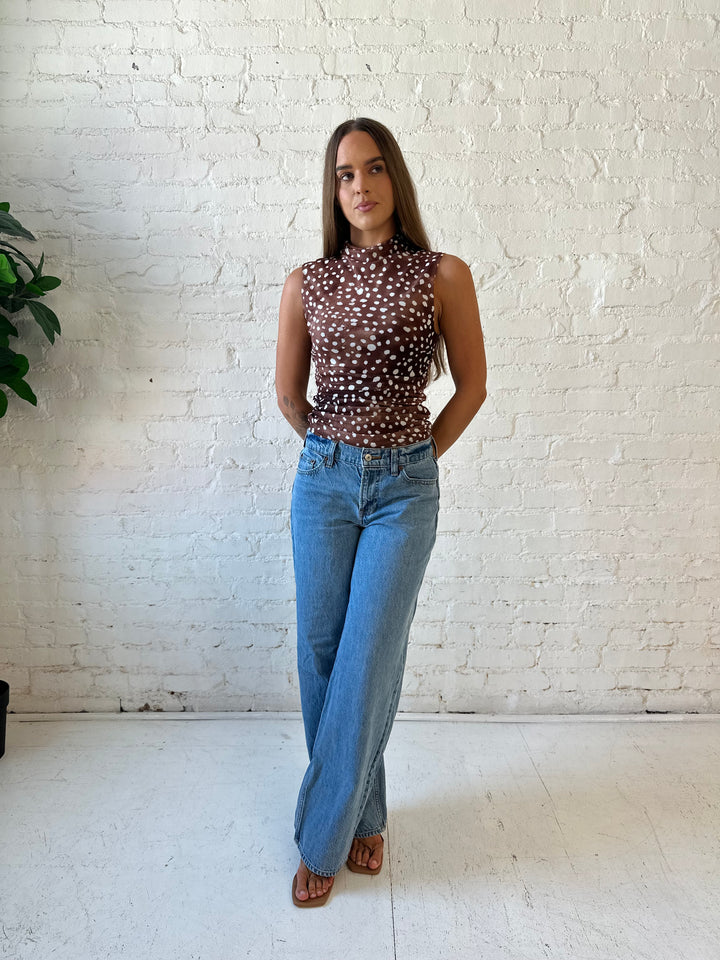 Woman wearing fawn print mesh sleeveless top with high neckline and medium wash jeans. 
