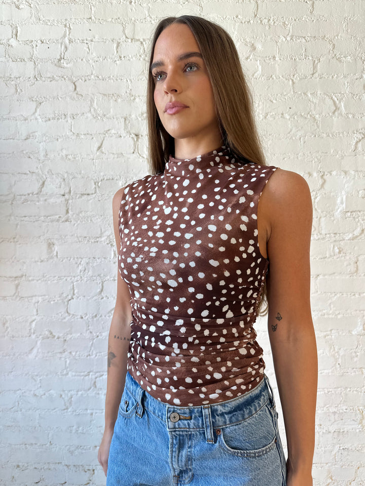 Woman wearing fawn print mesh sleeveless top with high neckline and medium wash jeans. 