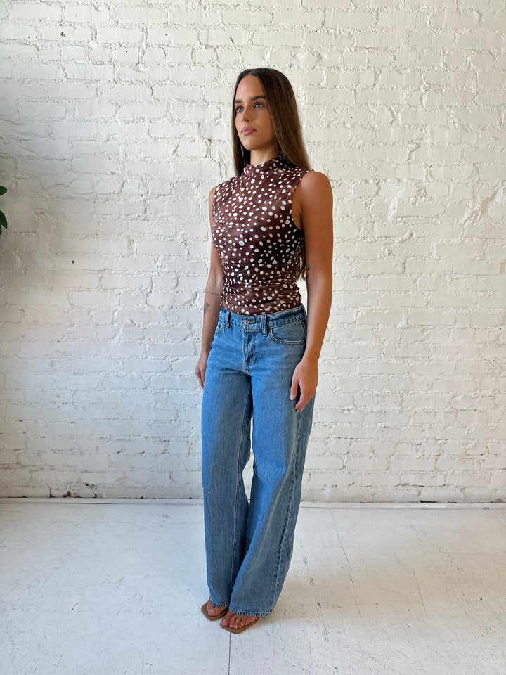 Woman wearing fawn print mesh sleeveless top with high neckline and medium wash jeans. 