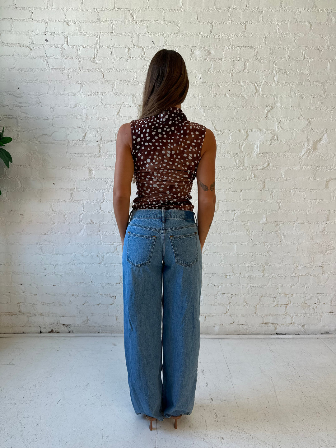 Woman wearing fawn print mesh sleeveless top with high neckline and medium wash jeans. 