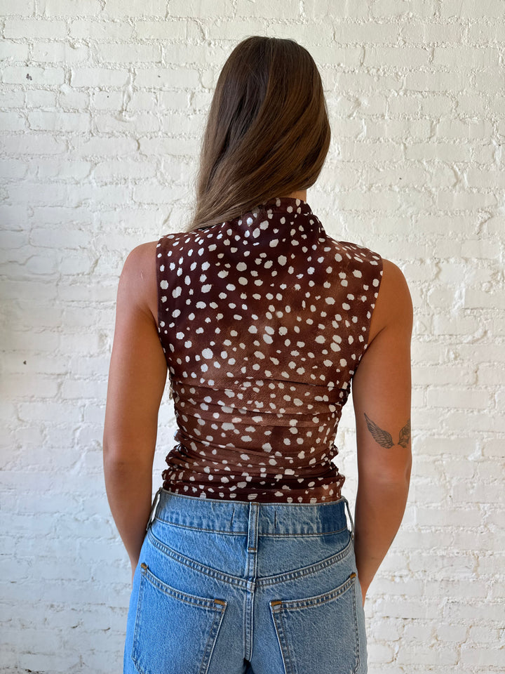 Woman wearing fawn print mesh sleeveless top with high neckline and medium wash jeans. 