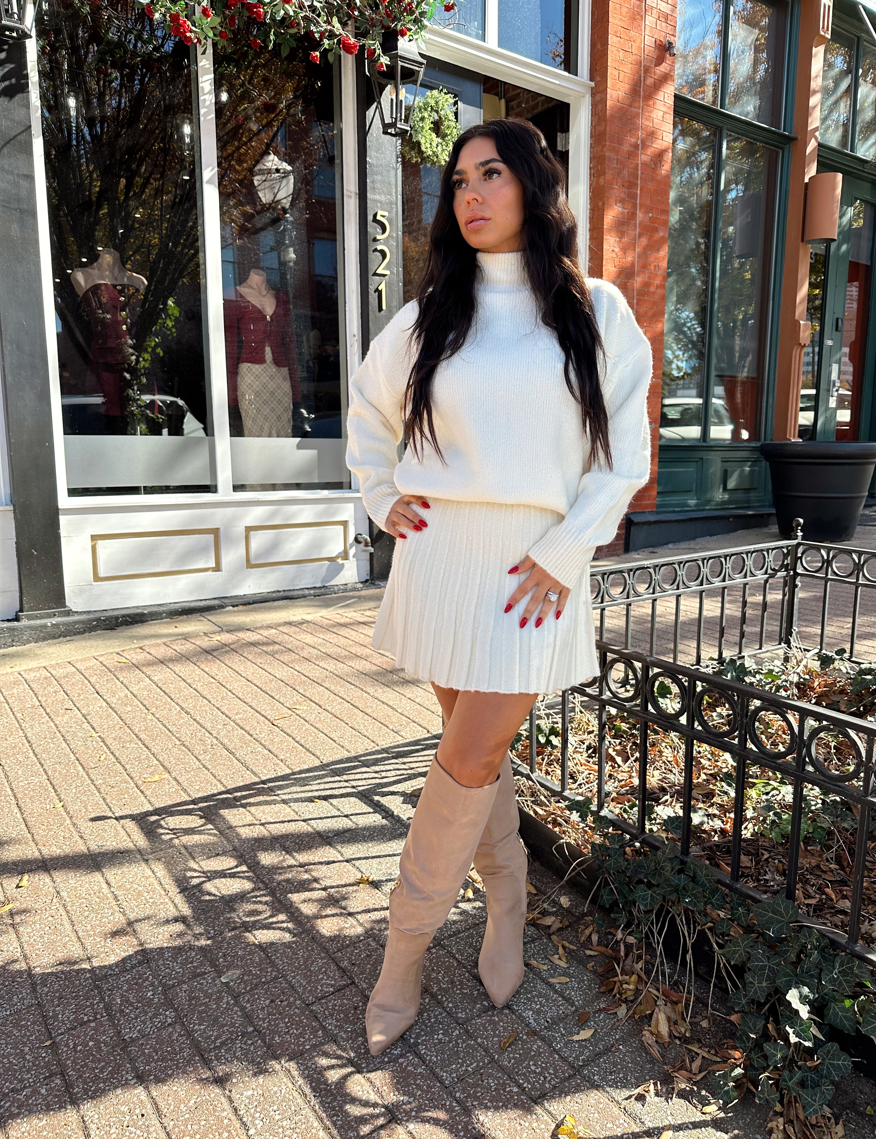 Woman wearing cream colored sweater set with pleated mini skirt. 