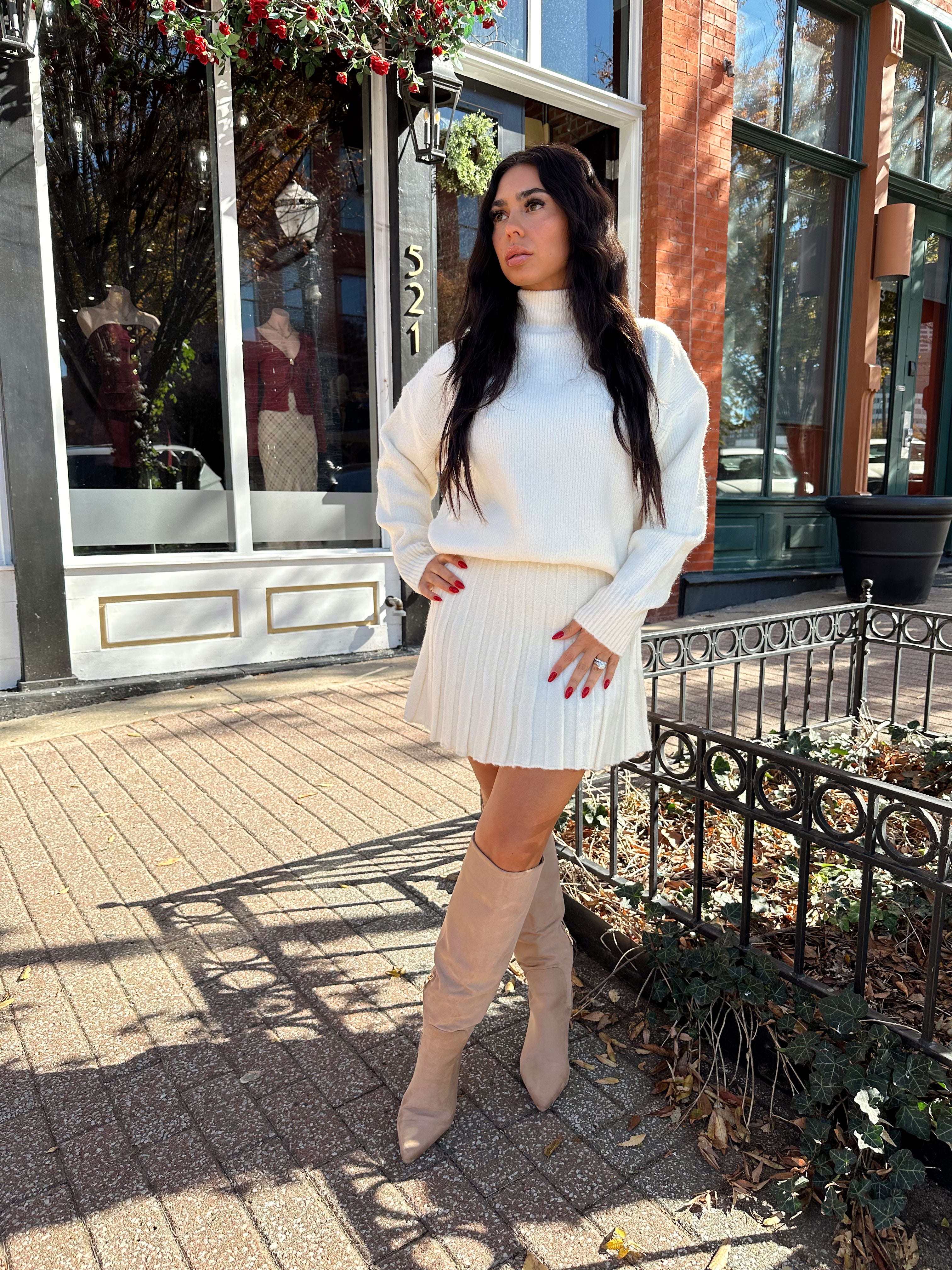 Woman wearing cream colored sweater set with pleated mini skirt. 