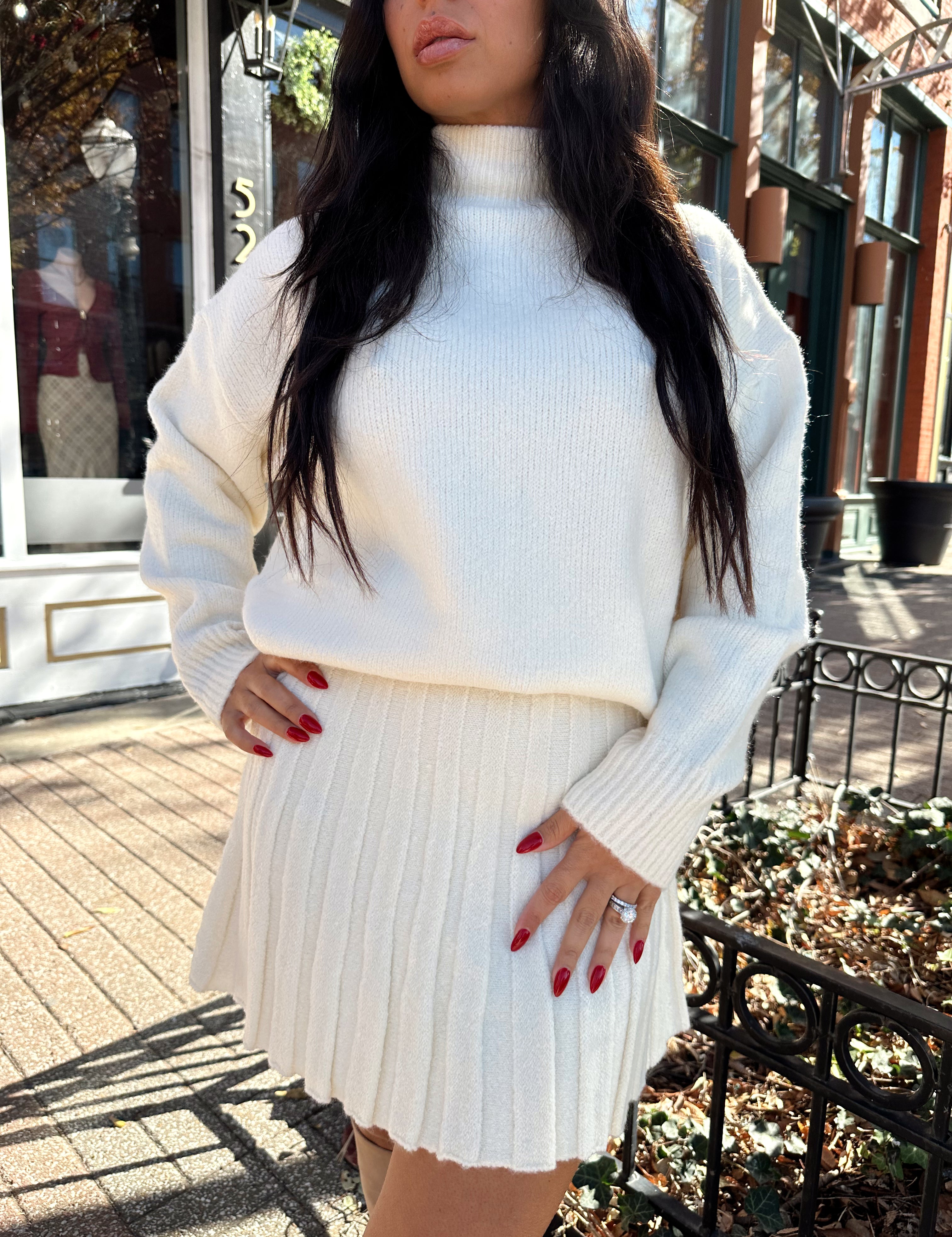 Woman wearing cream colored sweater set with pleated mini skirt. 