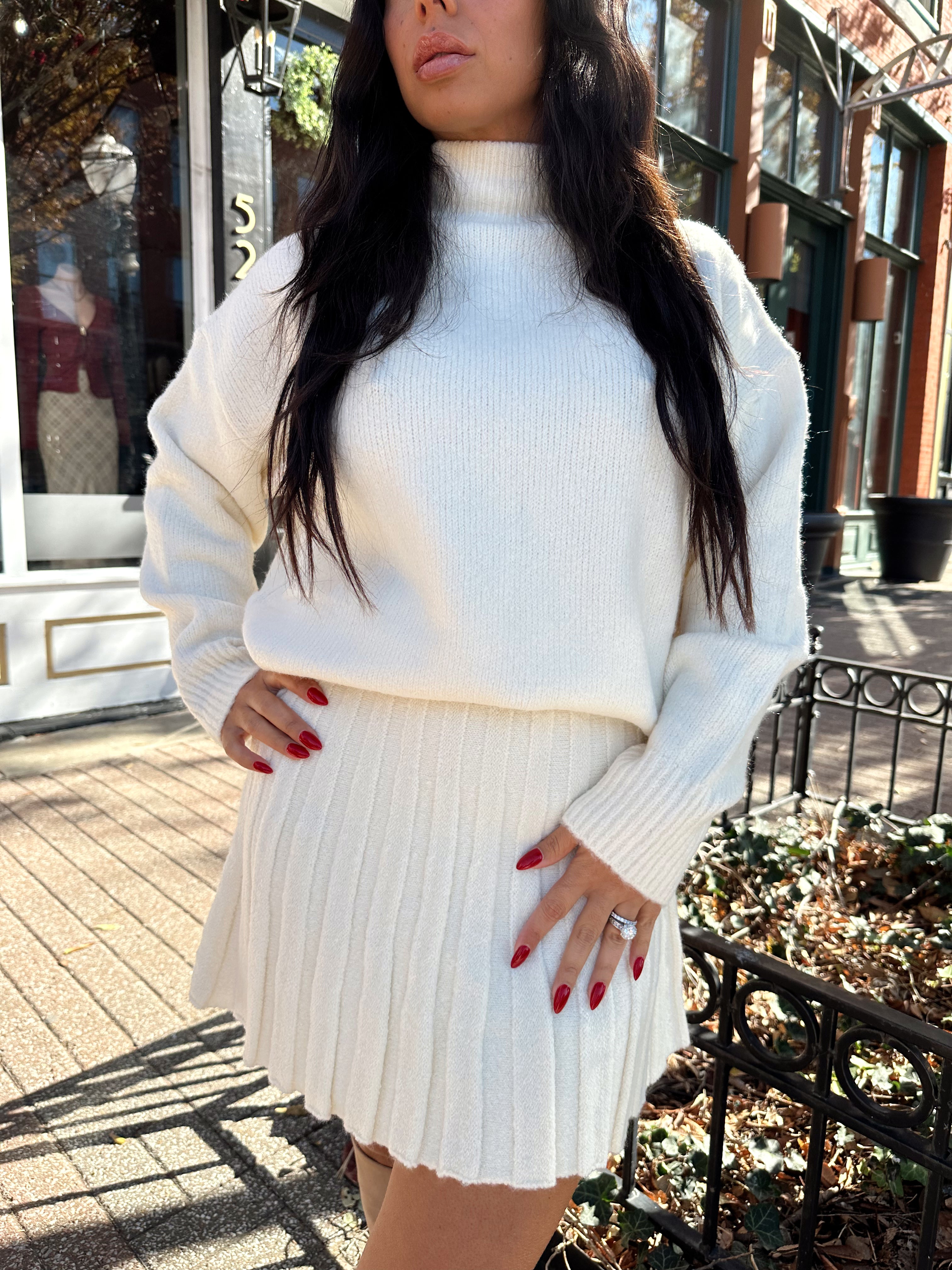Woman wearing cream colored sweater set with pleated mini skirt. 