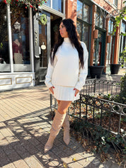Woman wearing cream colored sweater set with pleated mini skirt. 