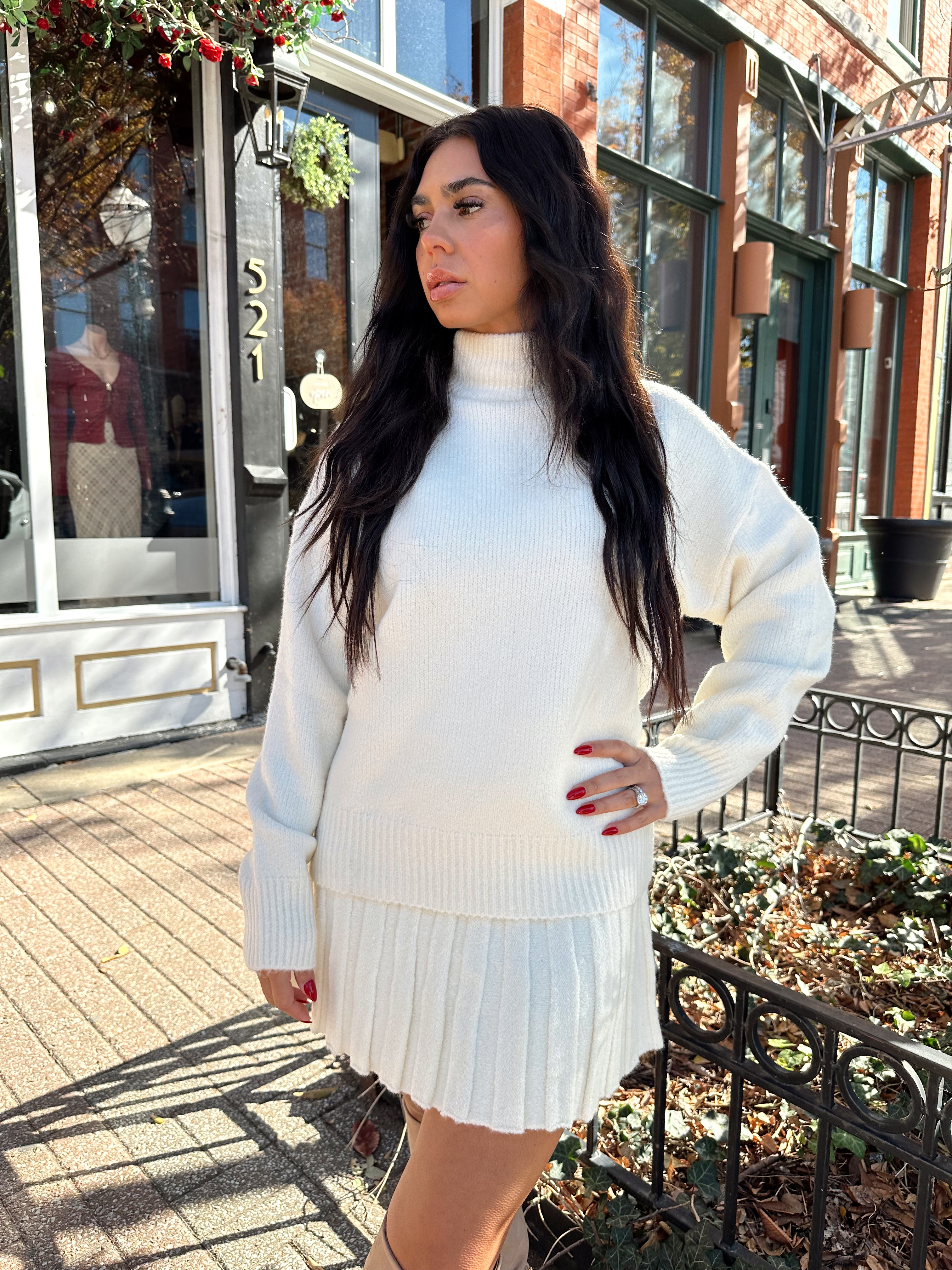 Woman wearing cream colored sweater set with pleated mini skirt. 