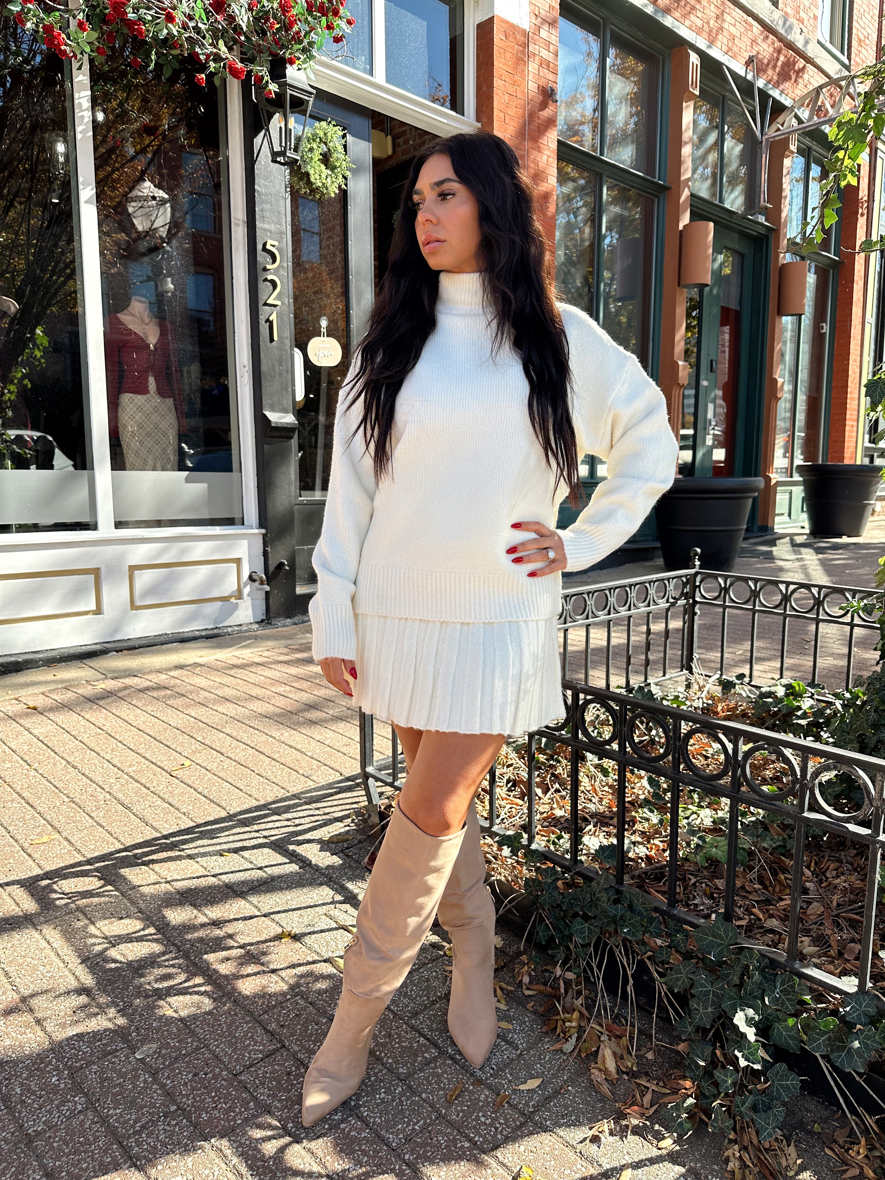 Woman wearing cream colored sweater set with pleated mini skirt. 