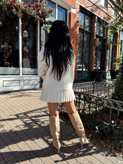Woman wearing cream colored sweater set with pleated mini skirt. 