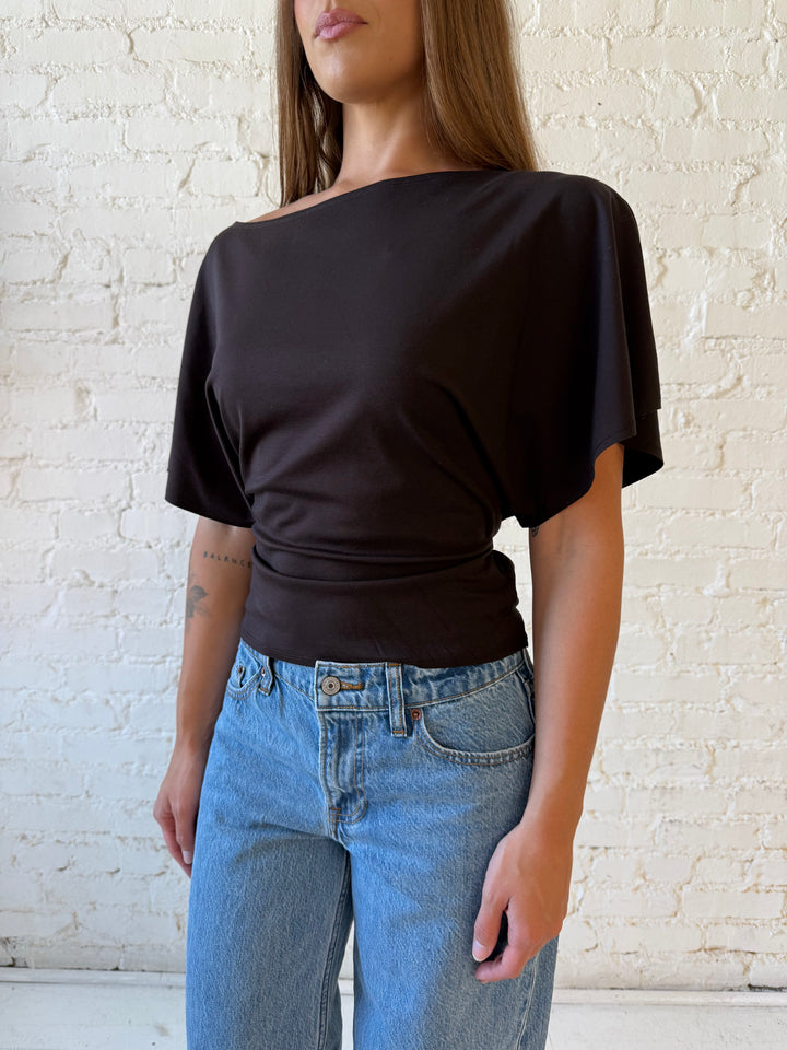 Woman wearing brown short sleeve fitted tie top with medium wash jeans. 