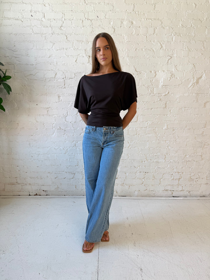 Woman wearing brown short sleeve fitted tie top with medium wash jeans. 