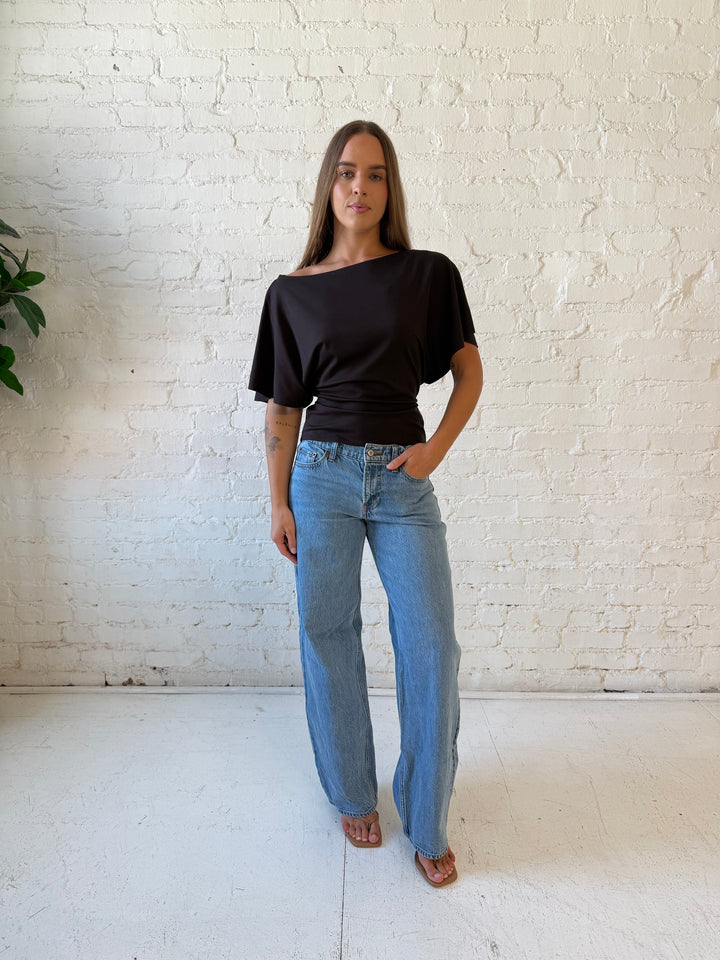 Woman wearing brown short sleeve fitted tie top with medium wash jeans. 