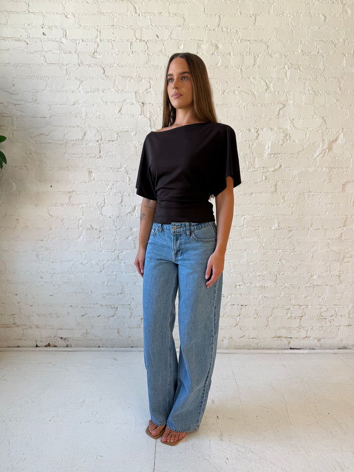 Woman wearing brown short sleeve fitted tie top with medium wash jeans. 