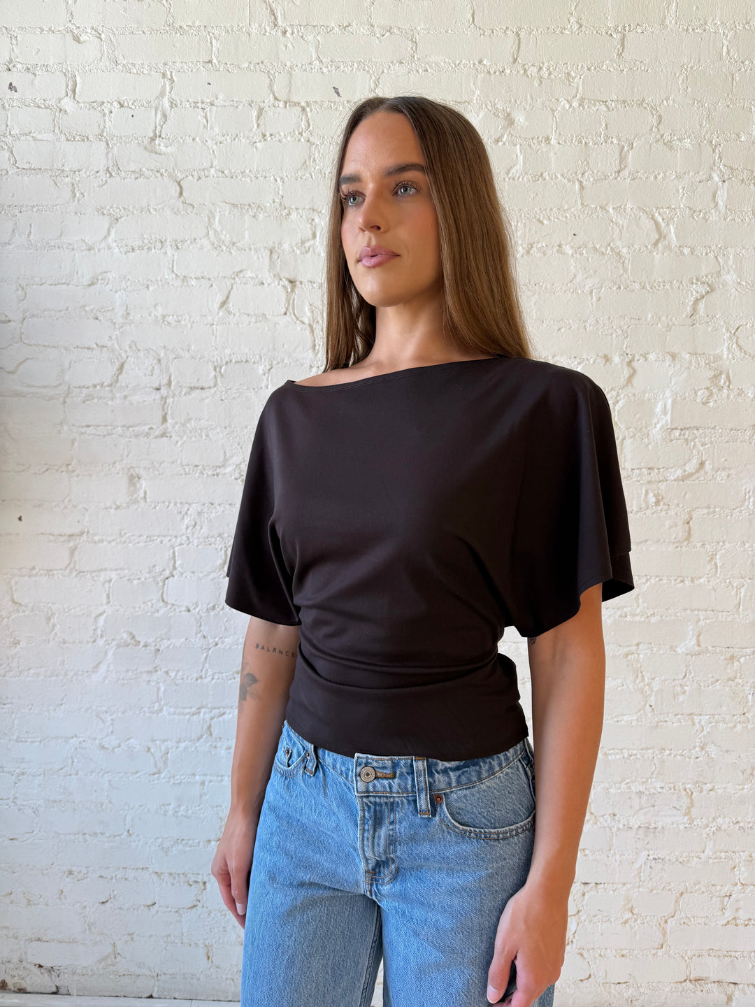 Woman wearing brown short sleeve fitted tie top with medium wash jeans. 