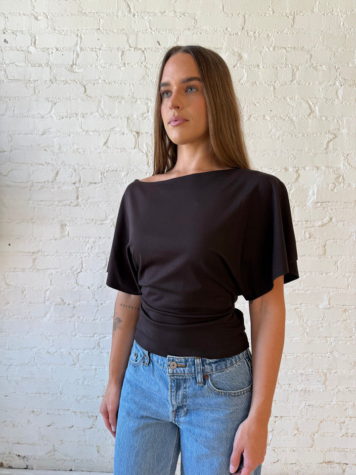 Woman wearing brown short sleeve fitted tie top with medium wash jeans. 