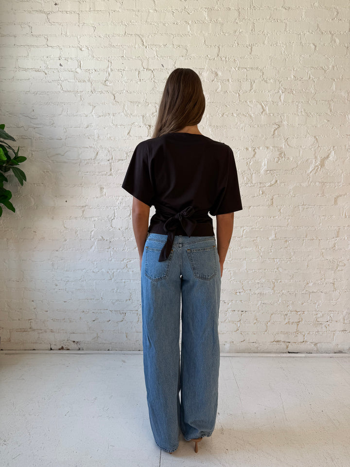 Woman wearing brown short sleeve fitted tie top with medium wash jeans. 