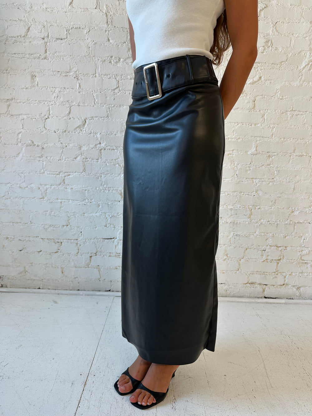 Woman wearing black faux leather midi skirt with belted waist and white cap sleeve top.