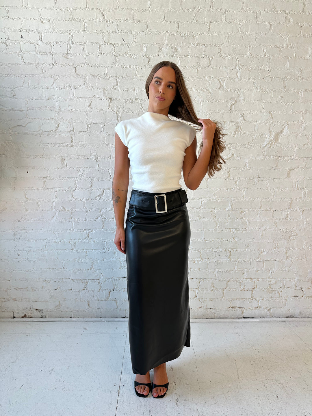 Woman wearing black faux leather midi skirt with belted waist and white cap sleeve top.