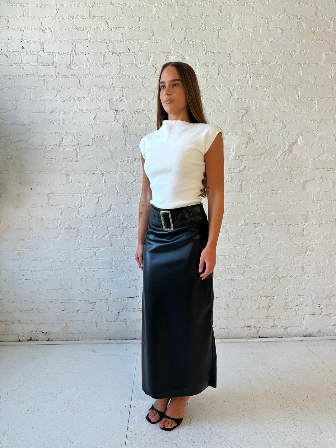 Woman wearing black faux leather midi skirt with belted waist and white cap sleeve top.