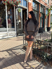 Woman wearing brown sweater two piece set with pleated mini skirt. 