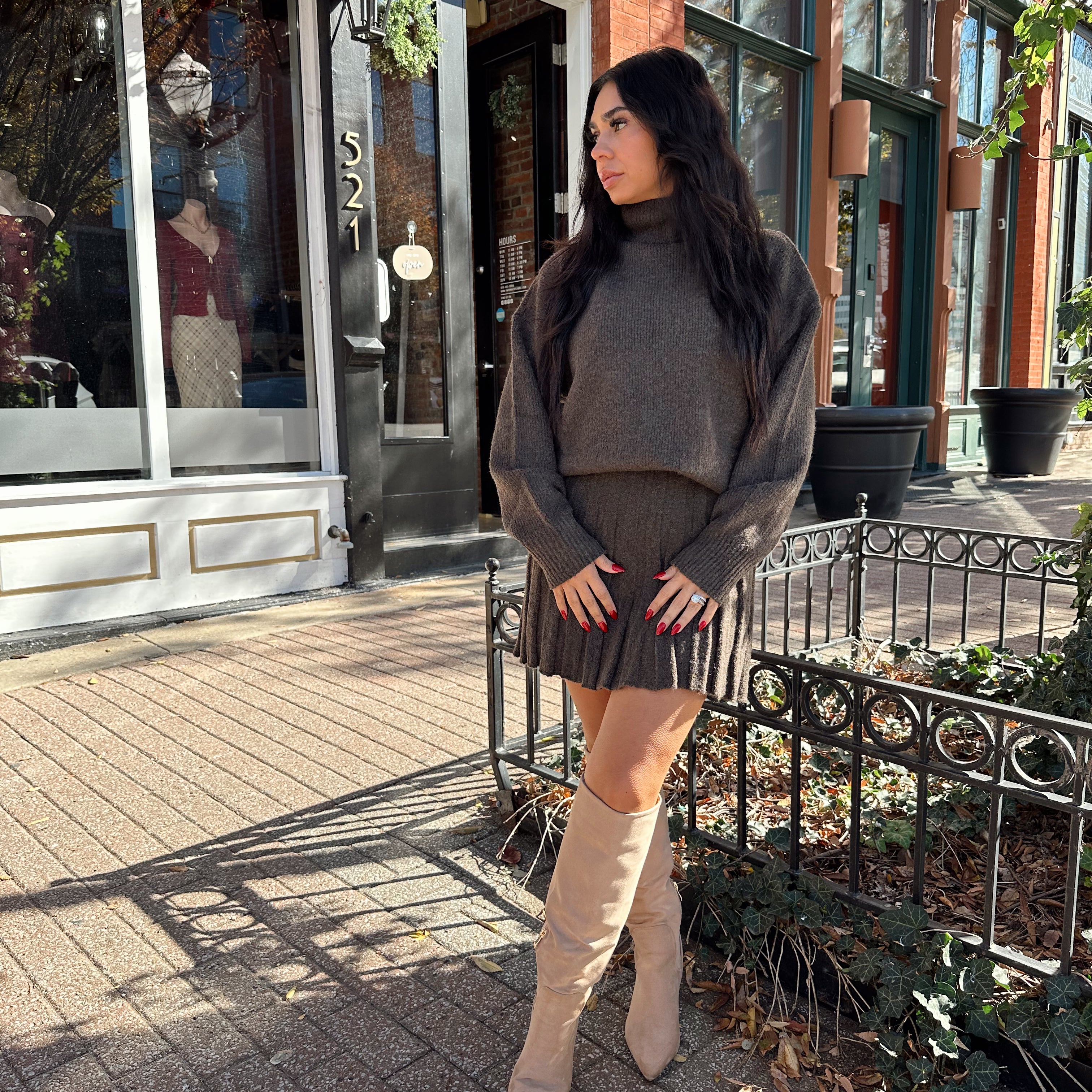 Woman wearing brown sweater two piece set with pleated mini skirt. 